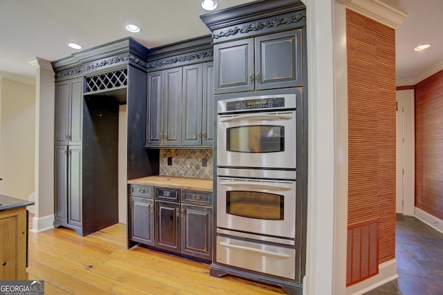 kitchen with crown molding, stainless steel double oven, decorative backsplash, and light hardwood / wood-style flooring