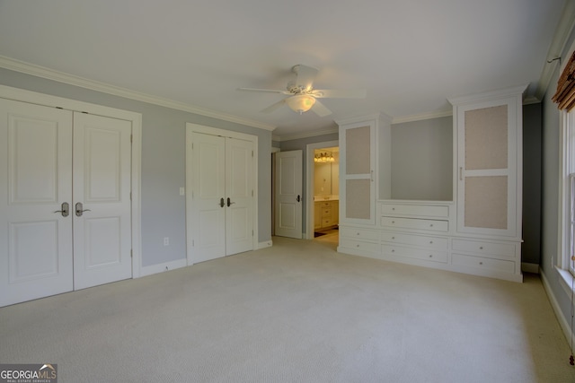 unfurnished bedroom featuring crown molding, ensuite bath, multiple closets, ceiling fan, and light colored carpet