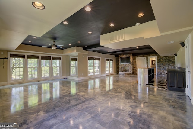 interior space featuring ceiling fan, a stone fireplace, and a raised ceiling