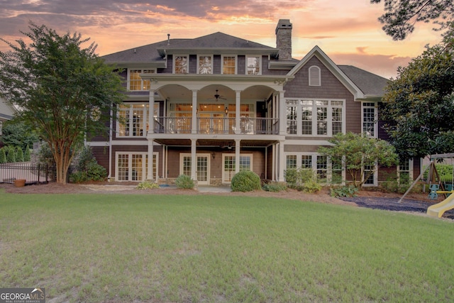 back house at dusk featuring ceiling fan, a balcony, and a yard