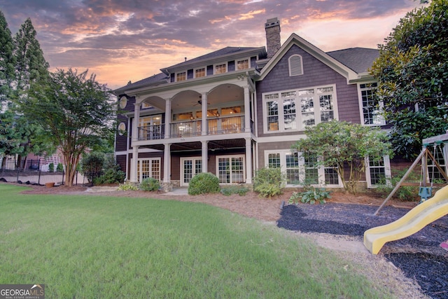 back house at dusk featuring a balcony, a yard, and a playground