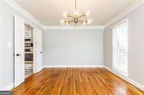 unfurnished dining area with crown molding, wood-type flooring, and an inviting chandelier