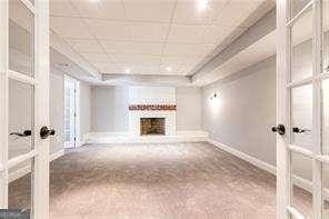 unfurnished living room featuring a raised ceiling, a brick fireplace, carpet, and french doors