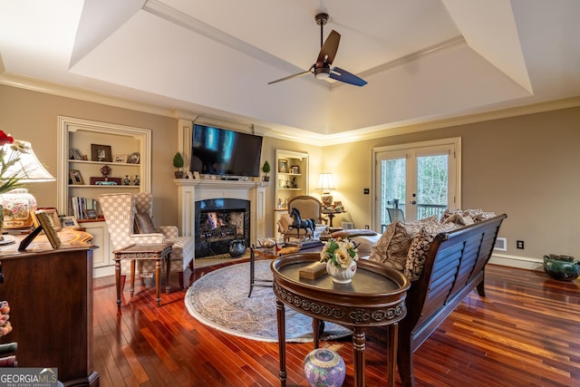 living room featuring dark wood-type flooring, crown molding, a tray ceiling, built in features, and a high end fireplace