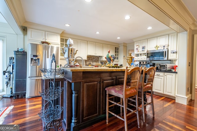 kitchen featuring stainless steel appliances, dark hardwood / wood-style floors, a breakfast bar, and an island with sink