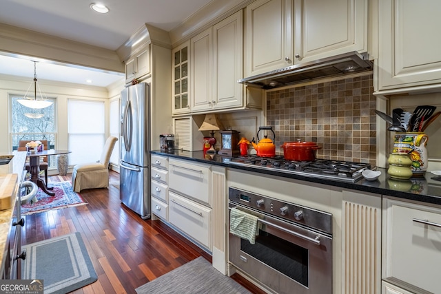 kitchen with appliances with stainless steel finishes, pendant lighting, tasteful backsplash, dark hardwood / wood-style flooring, and cream cabinets