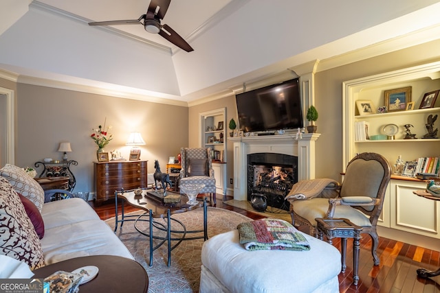 living room featuring built in shelves, crown molding, ceiling fan, a tiled fireplace, and hardwood / wood-style floors