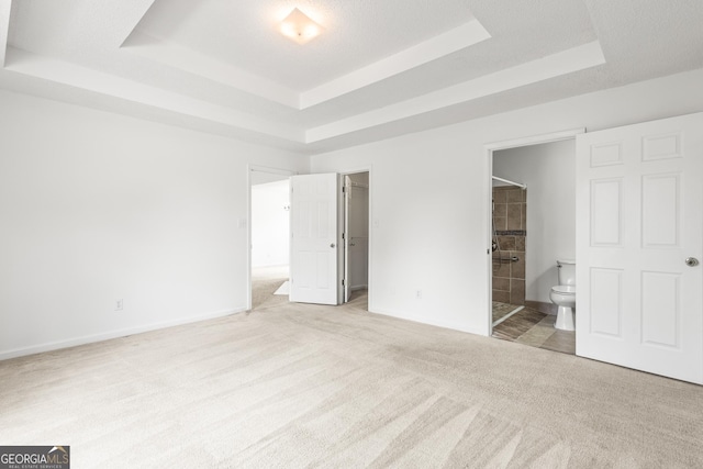 unfurnished bedroom featuring baseboards, connected bathroom, a tray ceiling, a walk in closet, and carpet flooring