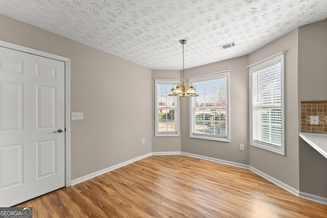 unfurnished dining area with a textured ceiling, wood-type flooring, and a chandelier