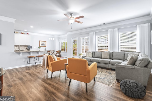 living area with visible vents, wood finished floors, crown molding, and ceiling fan with notable chandelier