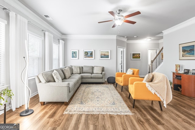 living area with visible vents, ornamental molding, a ceiling fan, wood finished floors, and stairway