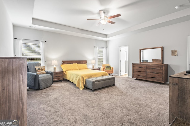 carpeted bedroom with a raised ceiling, visible vents, and ceiling fan