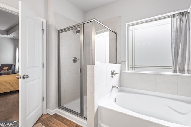 ensuite bathroom with a bath, a shower stall, ensuite bath, and wood finished floors