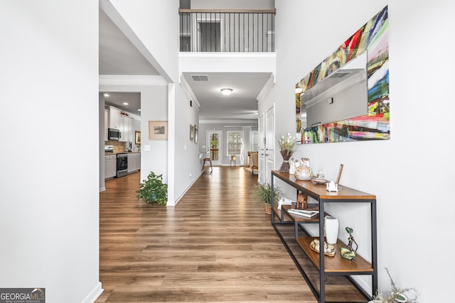 interior space with wood finished floors, visible vents, baseboards, a towering ceiling, and crown molding