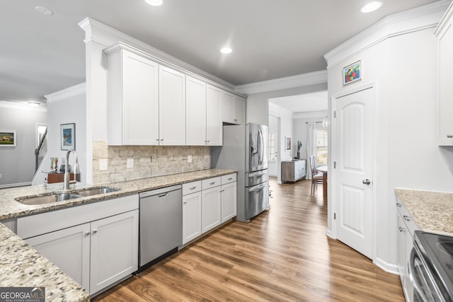 kitchen featuring light wood-style flooring, a sink, tasteful backsplash, appliances with stainless steel finishes, and crown molding