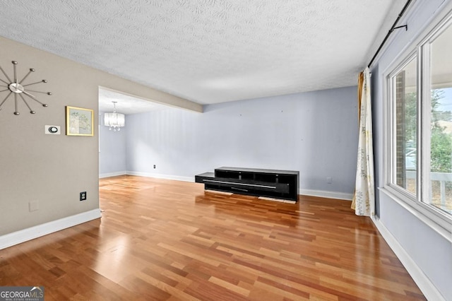 empty room featuring an inviting chandelier, wood-type flooring, and a textured ceiling