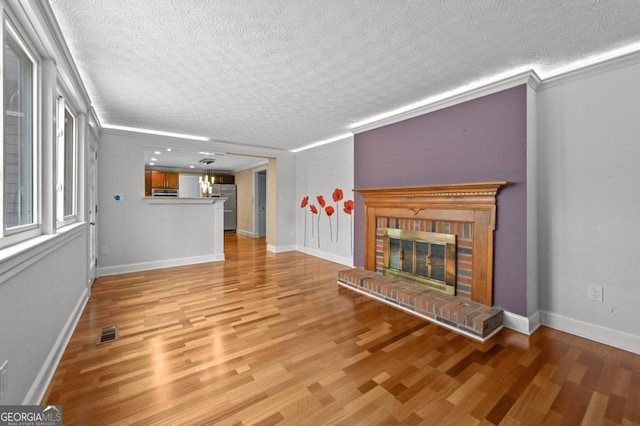 unfurnished living room with crown molding, light hardwood / wood-style floors, a brick fireplace, and a textured ceiling