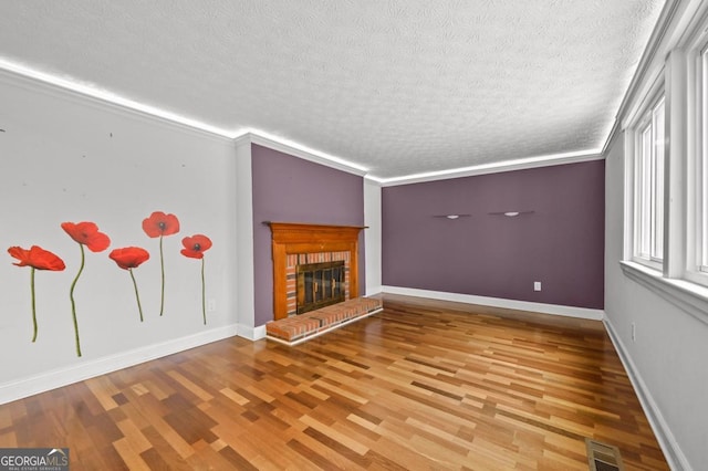 unfurnished living room featuring wood-type flooring, ornamental molding, a textured ceiling, and a fireplace