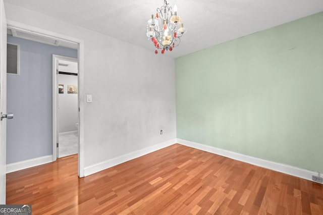 unfurnished room featuring an inviting chandelier and hardwood / wood-style floors