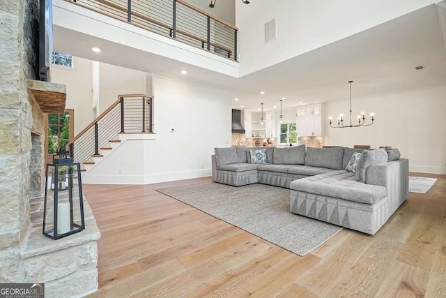 living room with baseboards, stairs, a high ceiling, light wood-type flooring, and a notable chandelier