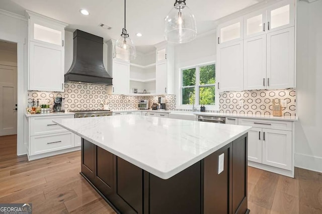 kitchen featuring glass insert cabinets, a center island, white cabinetry, and custom exhaust hood