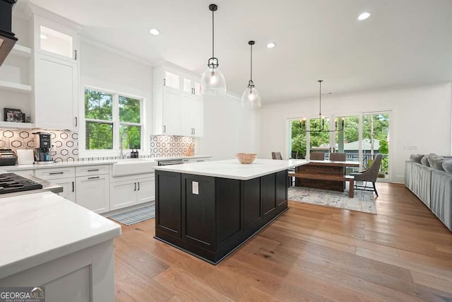 kitchen featuring a sink, white cabinets, light countertops, hanging light fixtures, and glass insert cabinets