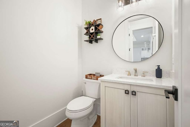 half bathroom featuring toilet, baseboards, and vanity