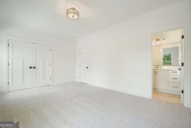 unfurnished bedroom with baseboards, ornamental molding, ensuite bath, and light colored carpet