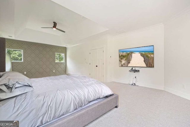 bedroom with an accent wall, a raised ceiling, light colored carpet, and baseboards