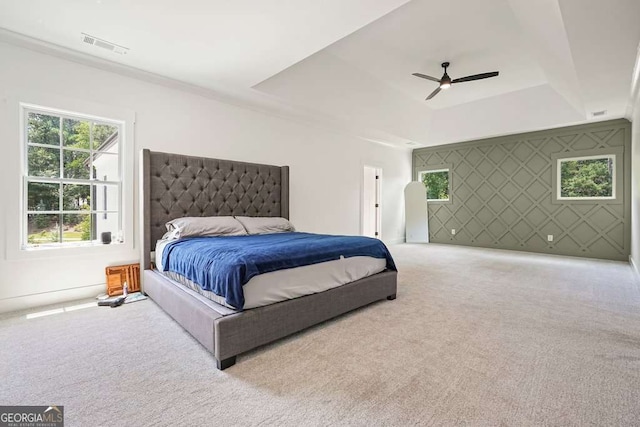 bedroom with light carpet, visible vents, a raised ceiling, a ceiling fan, and an accent wall