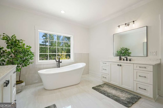 full bathroom with a wainscoted wall, tile walls, ornamental molding, vanity, and a freestanding tub