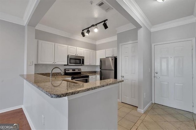 kitchen with dark stone counters, ornamental molding, kitchen peninsula, stainless steel appliances, and white cabinets