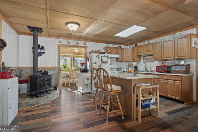 kitchen with a kitchen island, a wood stove, a breakfast bar area, sink, and dark hardwood / wood-style flooring