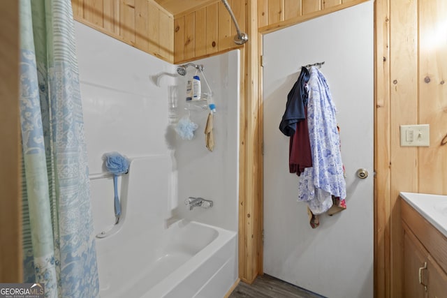 bathroom featuring hardwood / wood-style flooring, vanity, shower / bathtub combination with curtain, and wooden walls