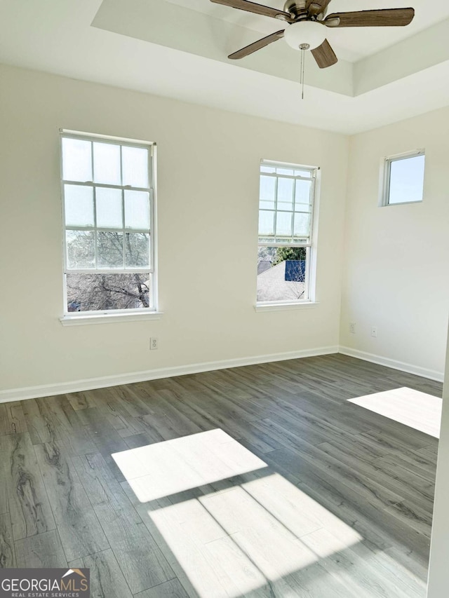 spare room featuring dark wood-type flooring, ceiling fan, plenty of natural light, and a raised ceiling