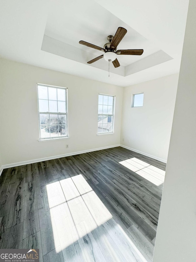 spare room with dark wood-type flooring, a raised ceiling, and ceiling fan