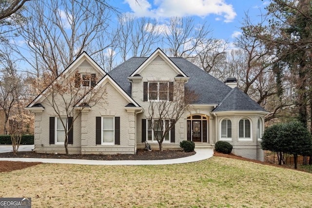 view of front of property with a chimney, brick siding, roof with shingles, and a front yard