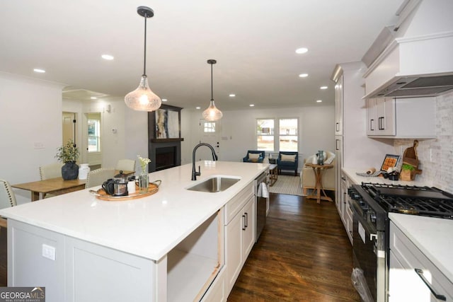 kitchen with black gas range oven, an island with sink, white cabinetry, sink, and custom exhaust hood