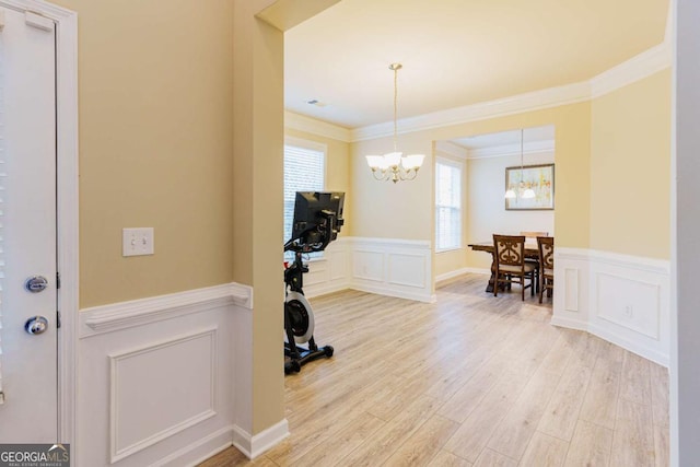 exercise room featuring ornamental molding, light hardwood / wood-style flooring, and a notable chandelier