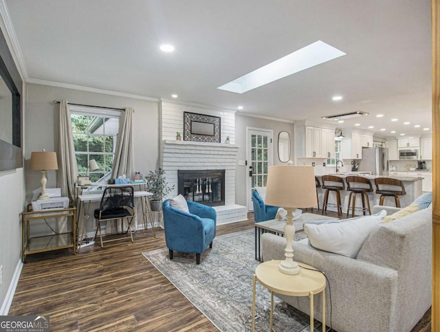 living room featuring crown molding, dark hardwood / wood-style flooring, a skylight, and a brick fireplace