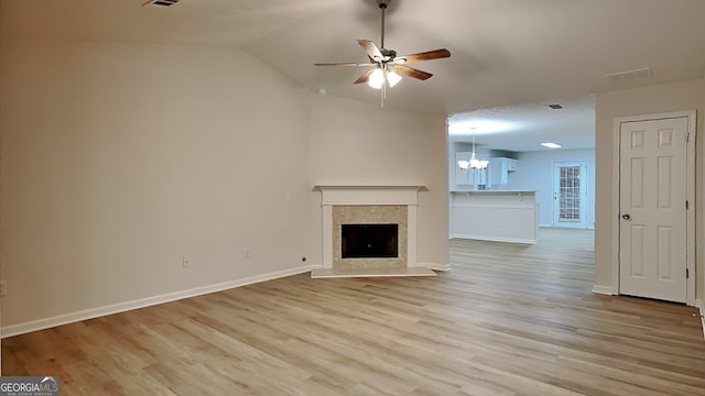 unfurnished living room with light hardwood / wood-style flooring, ceiling fan with notable chandelier, a high end fireplace, and vaulted ceiling