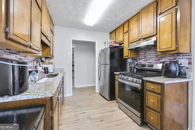 kitchen featuring tasteful backsplash, stainless steel appliances, light stone countertops, and light wood-type flooring