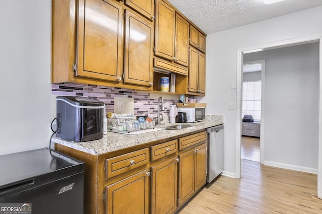 kitchen featuring sink, a textured ceiling, stainless steel dishwasher, light hardwood / wood-style floors, and decorative backsplash