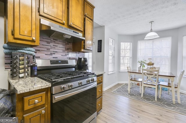 kitchen featuring tasteful backsplash, hanging light fixtures, stainless steel gas range oven, light stone countertops, and light hardwood / wood-style flooring