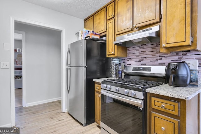 kitchen featuring stainless steel appliances, tasteful backsplash, light stone counters, light hardwood / wood-style floors, and a textured ceiling