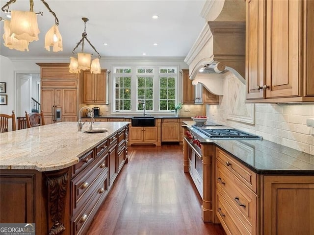 kitchen featuring pendant lighting, dark stone counters, sink, and a large island with sink