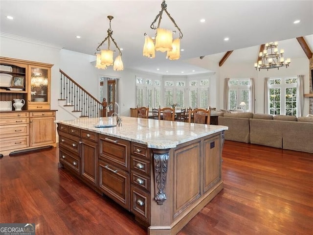 kitchen featuring decorative light fixtures, an island with sink, sink, light stone counters, and dark wood-type flooring