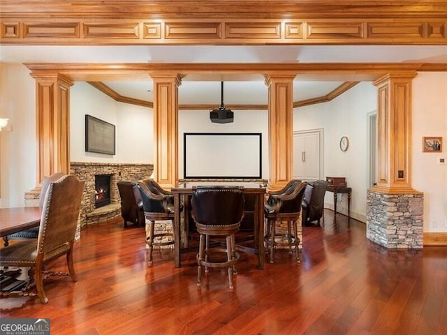 bar featuring dark wood-type flooring, ornamental molding, a fireplace, and decorative columns