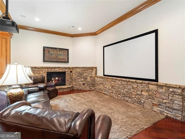 home theater room featuring crown molding, a stone fireplace, and dark wood-type flooring