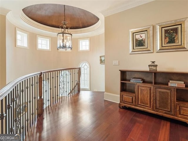 corridor with a raised ceiling, crown molding, dark hardwood / wood-style floors, and a chandelier